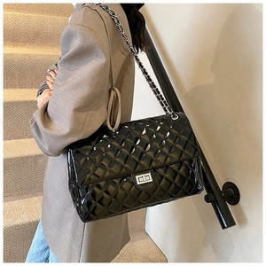 Detail of glossy black quilted chain bag with silver twist lock on model's shoulder