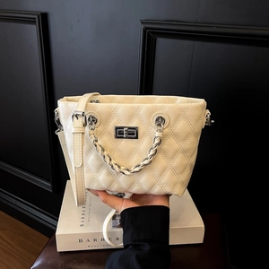 Detail of beige quilted leather bag showing silver twist lock and metal chain handle