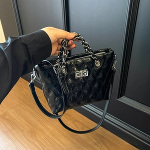 Macro view of black patent leather crossbody bag with diamond quilting and silver turn-lock