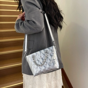 Silver quilted chain bag with metal lock shown on a model by wooden stairs