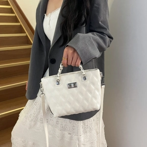 Detail of silver twist lock closure on a white quilted crossbody bag with metal chain