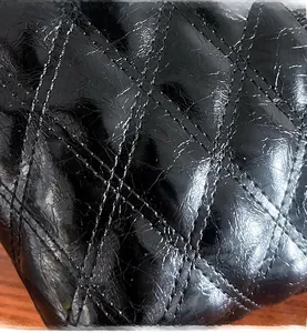 Close-up of glossy black quilted patent leather texture with diamond stitching on handbag