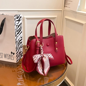 Red lychee pattern leather handbag with silk scarf and adjustable strap on a glass table