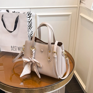 Elegant off-white lychee leather handbag with decorative silk scarf on glass table