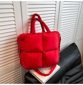 Détail du sac cabas matelassé rouge avec poignées épaisses sur un canapé en cuir