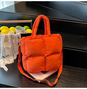 Détail d'un sac cabas orange vif en nylon matelassé sur un fond élégant en bois noir