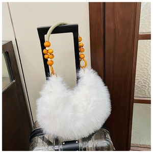 Close-up of white plush handbag with orange and beige beaded handle on a suitcase