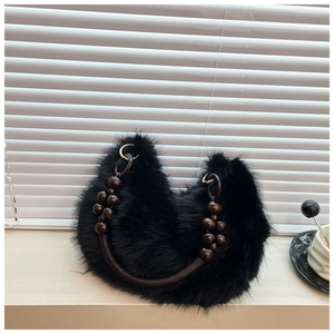 Detail of plush black faux fur bag with wooden bead handle and golden hardware on marble