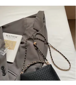 Detail of black woven leather shoulder bag with gold chain strap on a minimalist setup