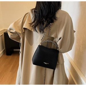 Detail of a black woven leather crossbody bag with chain strap on a model's shoulder