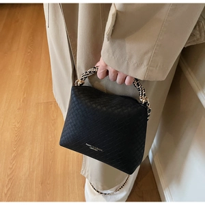 Detail of black woven leather handbag with gold chain handle and debossed brand lettering