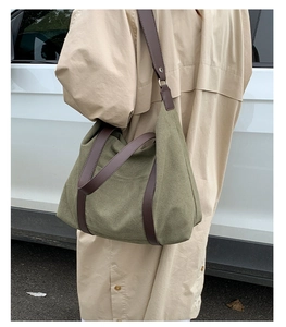 Détail du sac cabas en toile verte avec lanières en cuir marron porté sur un trench beige
