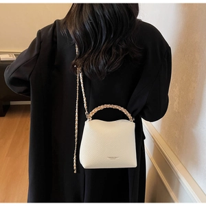 Detail of white quilted crossbody bag with gold chain strap and textured leather finish