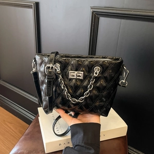 Chic black quilted crossbody bag with metal chain strap and twist lock on white box