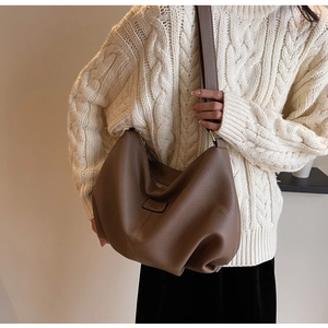 Braune Hobo-Tasche aus Leder mit Narbung und breitem Schultergurt auf weißem Pullover