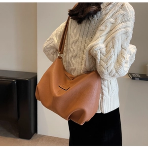 Detail einer braunen Shopper-Tasche aus Leder mit Narbenstruktur, getragen von einem Model