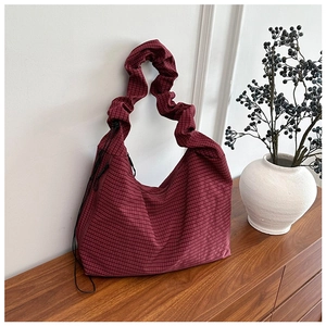Red checkered canvas bag with ruched strap detail leaning on wooden furniture