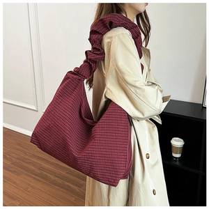 Detail of red checkered canvas tote bag with ruffled shoulder strap shown on model