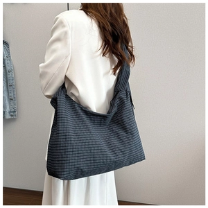 Close-up of a large black and gray checkered canvas tote bag worn by a model in soft light