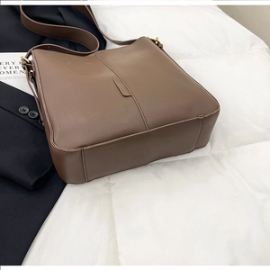 Close-up of brown matte leather tote bag with gold hardware on a quilted white surface