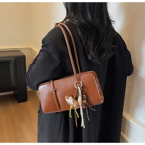 Sac sous le bras en similicuir marron avec pendentif en peluche et ruban porté par un mannequin