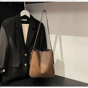 Detail of brown leather bucket bag with decorative stitching hanging next to a blazer
