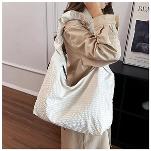 Detailed close-up of white crossbody bag with textured grid pattern and side drawstrings
