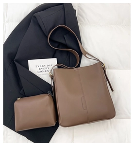 Close-up of brown leather tote bag set with matching zipper pouch on white quilted surface