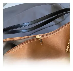 Detail of brown suede handbag with golden zipper, pearl accents, and metal chain strap