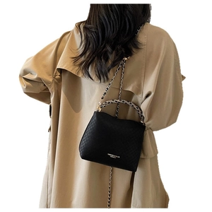 Classic black woven crossbody bag with chain strap shown on a model in a trench coat