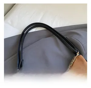 Detail of brown faux suede tote bag featuring black handles and gold chain accents