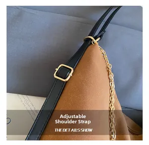 Close-up of adjustable black leather shoulder strap with gold hardware and chain on brown bag