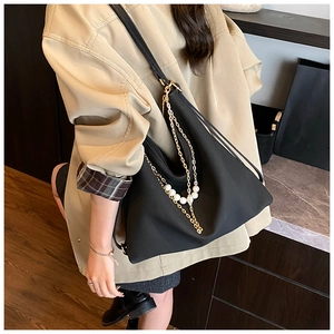 Detail of black nylon tote bag featuring gold chain strap and elegant pearl charm detail