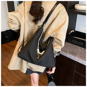 Detail of black large capacity shoulder bag with gold chain and white pearl accents
