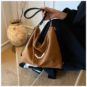 Close-up of brown suede handbag featuring elegant gold chains and white pearl details