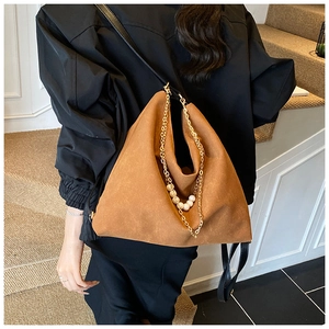 Brown suede shoulder bag featuring a gold chain and pearl accent on a model's outfit