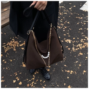 Detail of a brown large capacity shoulder bag with gold chain and white pearl accents