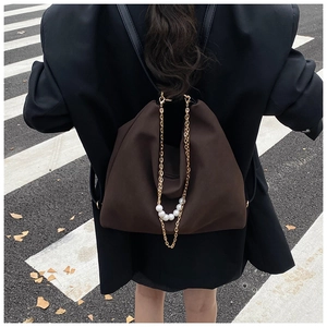 Street style view of deep brown fabric backpack with gold chain and pearl decoration