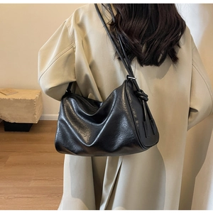 Close-up of black glossy leather Boston bag with side knot details on beige coat model