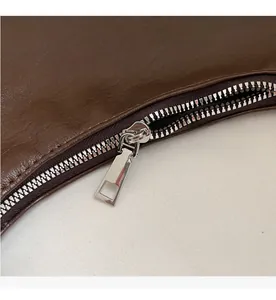 Close-up of smooth silver metal zipper on thick dark brown leather commuter bag