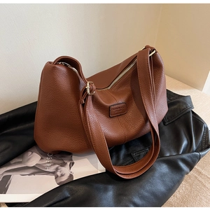 Braune Hobo-Tasche aus Leder mit breitem Gurt und Modelogo auf einer schicken Zeitschrift
