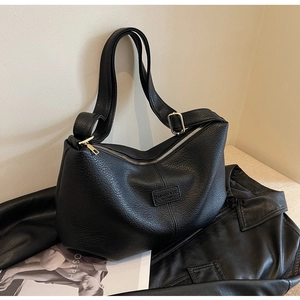 Schicke schwarze Handtasche mit Lychee-Muster und verstellbarem Gurt auf Lederjacke