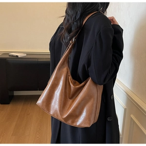 Side view of a vintage brown leather hobo bag with a wide shoulder strap on a model
