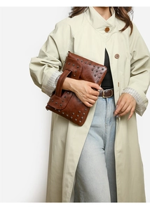 Nahaufnahme der braunen Vintage-Leder-Umschlagtasche mit quadratischen Nieten auf beigem Mantel