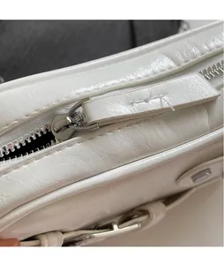 Détail du sac blanc en similicuir plissé montrant le zip argenté et la longue tirette