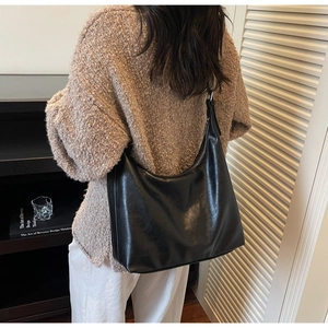 Detail of a large black glossy shoulder bag with zipper and wide strap shown on a model