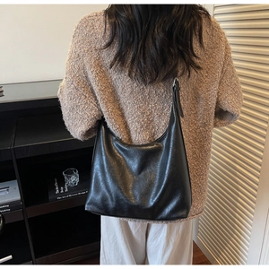 Detailed view of black minimalist hobo bag worn over the shoulder on a brown sweater