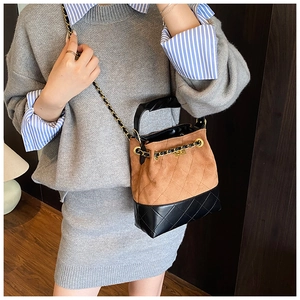 Detail of a brown suede and black leather bucket bag with quilted patterns and golden chain