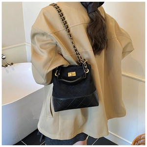 Detail of black quilted bucket bag featuring a gold chain strap and metal turn-lock closure