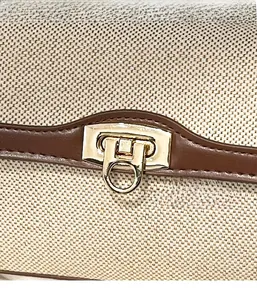 Detail of golden metal twist lock on beige canvas shoulder bag with brown leather trim